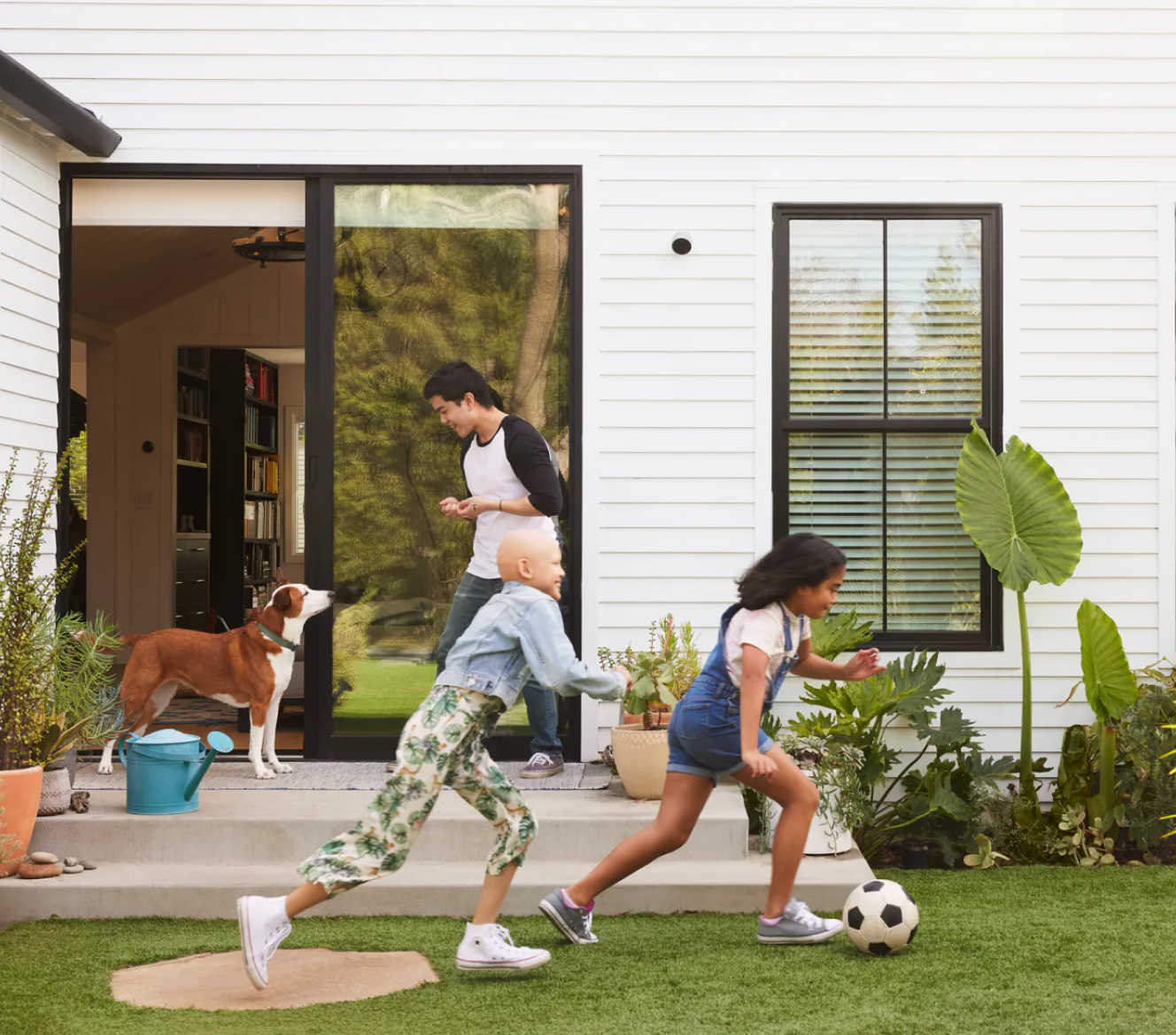 Family playing in the yard with a Google Nest Cam (outdoor or indoor, battery) installed on their home