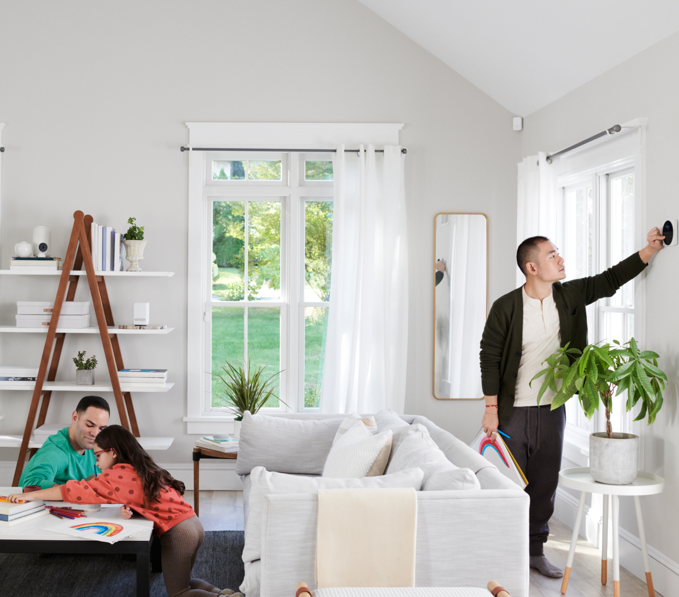 Man adjusting Google Nest Cam (indoor) in his home while his family colors with markers