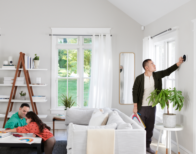 Man adjusting Google Nest Cam (indoor) in his home while his family colors with markers